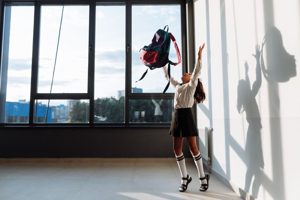 Girl in school uniform happily throwing her backpack